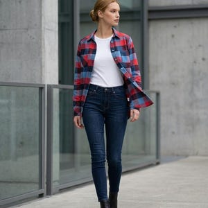 Peut inclure: Une femme porte une chemise à carreaux rouge, bleu et noir sur un t-shirt blanc, associée à un jean bleu foncé et des bottines noires. La tenue est décontractée et adaptée au quotidien.