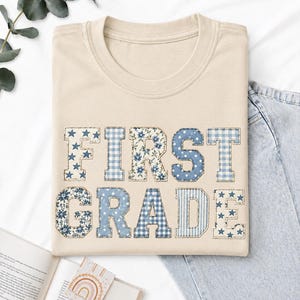 Può includere: Una t-shirt beige con la scritta FIRST GRADE in stile patchwork. Ogni lettera è riempita con diversi motivi blu e bianchi, tra cui stelle, stampe floreali, pois e quadretti vichy, creando un aspetto strutturato e stratificato.