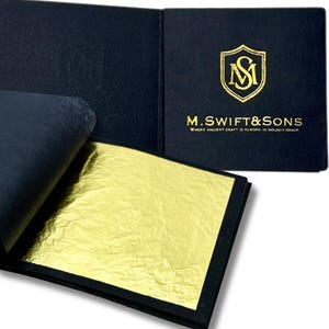 May include: A gold leaf sheet is displayed within a black folio. The folio is open, revealing the gold leaf and the embossed text "M. Swift & Sons" with a gold emblem. The gold leaf has a textured, crinkled appearance.