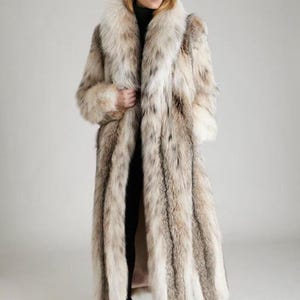 May include: A full-length, long-sleeved coat featuring a thick, voluminous fur collar and a textured, multi-tonal pattern of cream, beige, and dark brown vertical stripes. The garment is worn over a black turtleneck and black trousers with black heels.