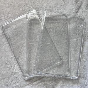 Puede incluir: Fundas transparentes para teléfonos. Las fundas están hechas de un material plástico transparente y están diseñadas para proteger el teléfono de arañazos y daños. Las fundas son de forma rectangular y tienen un borde elevado para proteger la pantalla.