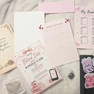 May include: A collection of stationery items with a romantic theme. Includes a book list, book review sheet, stickers, and a card that says "Your Blind Date with a Kindle Case". The color palette is soft pink and white.