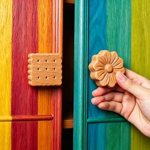 May include: Wooden cabinet knobs shaped like a biscuit and a flower. The light brown knobs are mounted on rainbow-striped cabinet doors. The doors are painted with vertical stripes of yellow, red, orange, blue, and green.