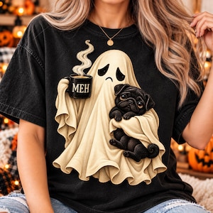 May include: A black t-shirt featuring a graphic of a cream-coloured ghost with a sad expression. The ghost holds a black mug with the text MEH printed in gold and carries a small black pug puppy wrapped within its flowing, draped fabric.