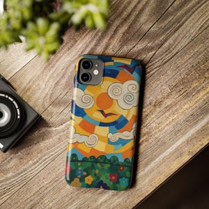 Peut inclure: Une coque de téléphone colorée avec une illustration vive d'un soleil, de nuages et d'oiseaux. Le design comprend des nuances de jaune, d'orange, de bleu et de vert. La coque est sur une surface en bois.