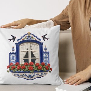 May include: A white square throw pillow featuring a centered illustration of a blue and white arched window frame with lace curtains, surrounded by blue and white patterned tiles, vibrant red geranium flowers, and two black swallows in flight.