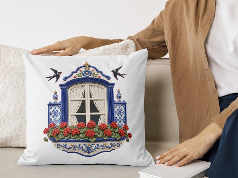 May include: A white square throw pillow featuring a centered illustration of a blue and white arched window frame with lace curtains, surrounded by blue and white patterned tiles, vibrant red geranium flowers, and two black swallows in flight.