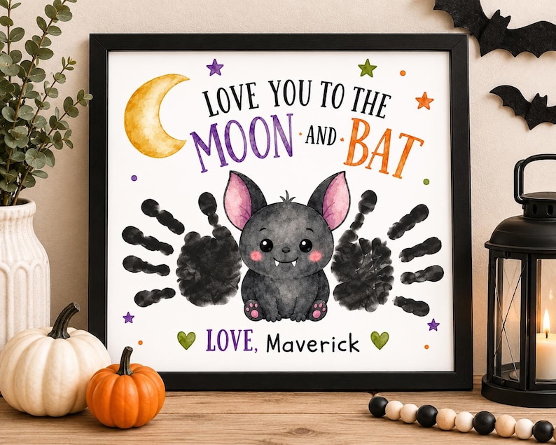 Puede incluir: Una impresi&oacute;n enmarcada con un murci&eacute;lago de dibujos animados con orejas rosas y dos alas de huellas de manos negras. El texto dice LOVE YOU TO THE MOON AND BAT y LOVE, Maverick. El dise&ntilde;o incluye una luna creciente amarilla y corazones verdes.