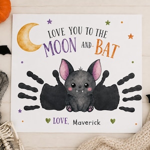 Puede incluir: Una l&aacute;mina cuadrada blanca con una ilustraci&oacute;n en acuarela de un murci&eacute;lago gris con orejas rosas. El texto dice LOVE YOU TO THE MOON AND BAT y LOVE, MAVERICK. Dos huellas de manos negras forman las alas, junto a una luna de color amarillo.