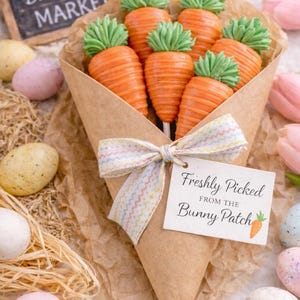 May include: A bouquet of carrot-shaped treats with green tops, wrapped in brown paper and tied with a pastel ribbon. A tag reads "Freshly Picked from the Bunny Patch." Easter eggs and a chalkboard sign are in the background.