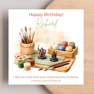 May include: A square greeting card featuring a watercolour illustration of miniature painting supplies, including brushes in a wooden cup, paint pots, and two painted figures. Text reads: Happy Birthday! Richard. I like you more than your unpainted pile of shame. And that's saying something.