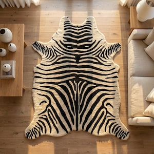 May include: A large, irregularly shaped area rug featuring a high-contrast black and white zebra stripe pattern. The rug has a soft, textured appearance and mimics the organic, asymmetrical silhouette of an animal hide, covering the floor space.
