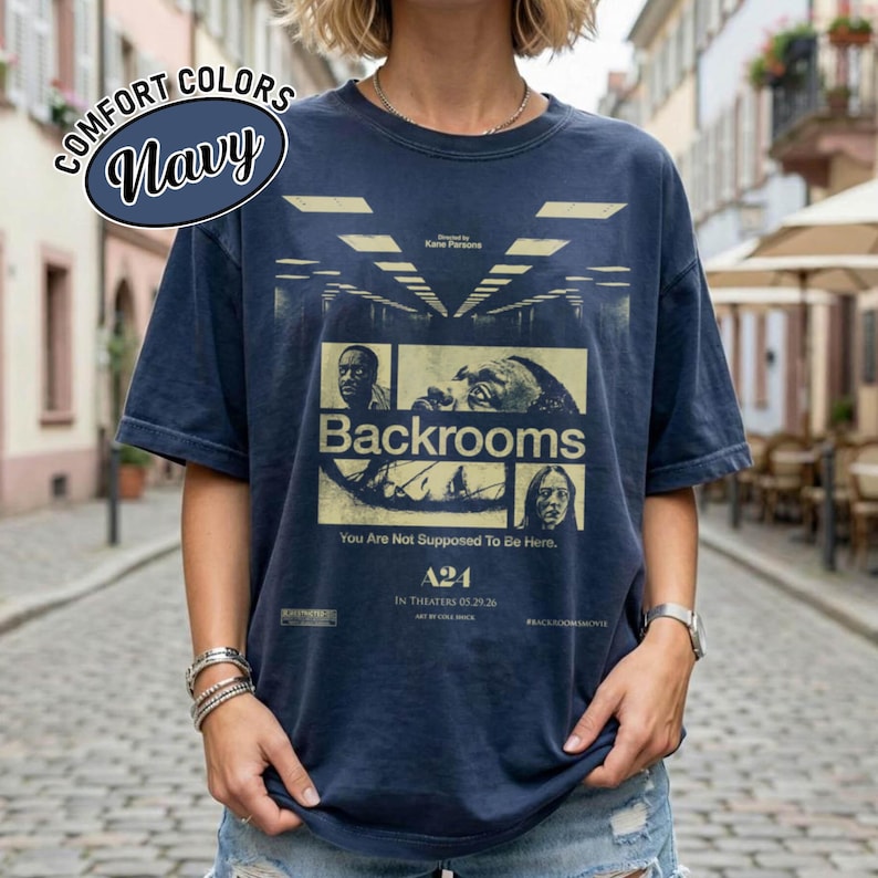Może przedstawiać: Granatowa koszulka z kr&oacute;tkim rękawem z nadrukiem graficznym plakatu filmowego Backrooms. Projekt zawiera obrazy w odcieniach ż&oacute;łci oraz tekst Backrooms, You Are Not Supposed To Be Here, A24 i In Theaters 05.29.26 na przedniej stronie.