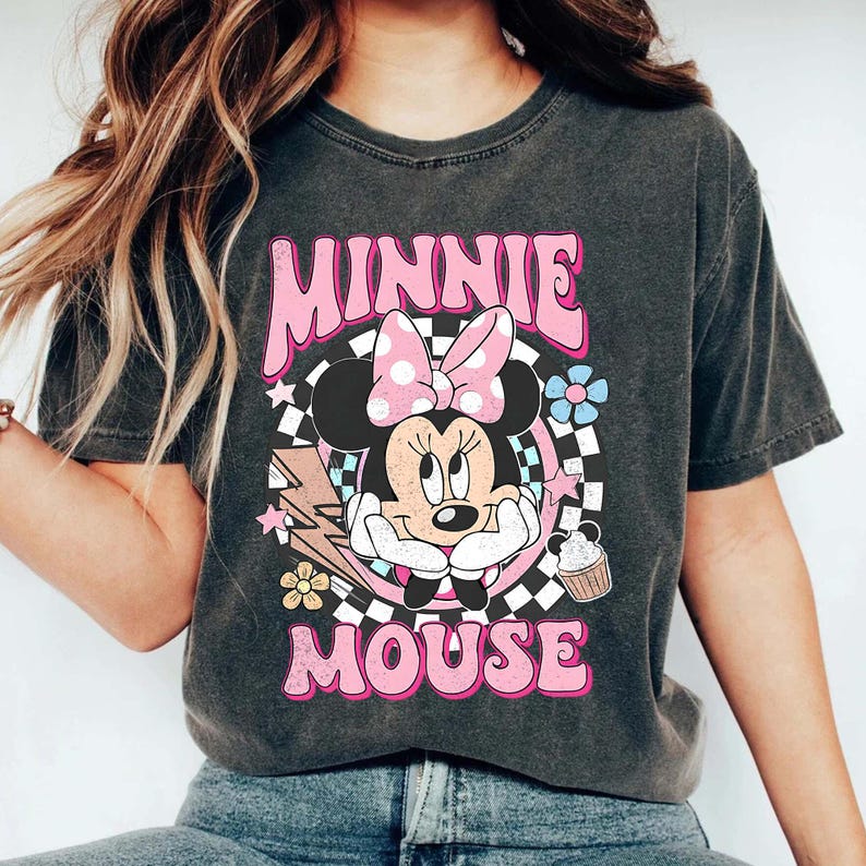 May include: Dark grey t-shirt with a graphic of Minnie Mouse wearing a pink polka dot bow, and the words "MINNIE MOUSE" in pink. The design includes flowers, a lightning bolt, and a cupcake.