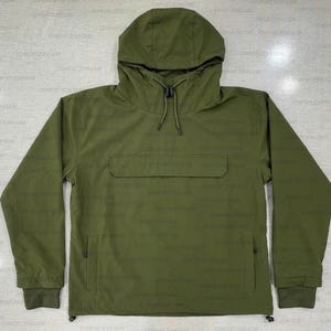 May include: An olive green anorak jacket featuring a hood and a front pocket. The jacket has long sleeves with ribbed cuffs and a drawstring at the hood. The anorak is made of a durable, water-resistant material.