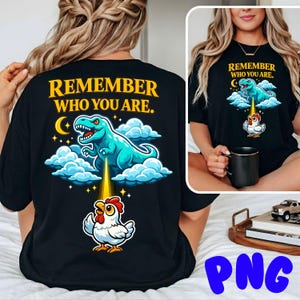 Puede incluir: Camiseta negra con el texto "REMEMBER WHO YOU ARE." y un dibujo animado de un dinosaurio azul, nubes y un pollo. El dinosaurio emite un rayo de luz hacia el pollo. El diseño incluye una luna creciente y estrellas.