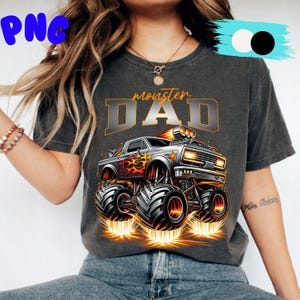 Pode incluir: T-shirt cinza escuro com um design de monster truck e o texto "monster DAD". O caminh&atilde;o &eacute; prateado com chamas laranja e pneus pretos grandes. O design inclui detalhes em laranja e amarelo, criando um gr&aacute;fico din&acirc;mico e atraente.