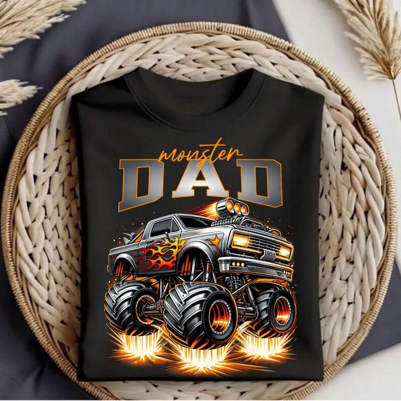 Pode incluir: Camiseta preta com um design de monster truck e o texto "monster DAD" em laranja e cinza. O design apresenta um monster truck detalhado com chamas e pneus grandes.