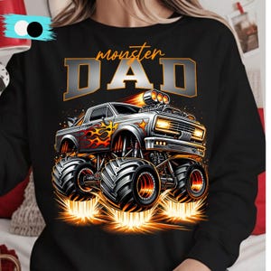 Pode incluir: Camisola preta com um design de monster truck com chamas e o texto "monster DAD" em laranja e cinza. O caminh&atilde;o tem pneus grandes e emite fa&iacute;scas, criando um design din&acirc;mico.