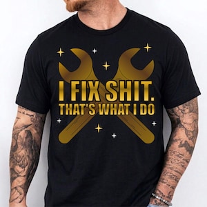 Puede incluir: Camiseta negra con un gráfico de llave inglesa dorada y el texto "I FIX SHIT. THAT'S WHAT I DO." El diseño incluye pequeños acentos de estrellas. Un diseño casual y humorístico.