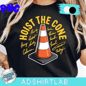 May include: Black t-shirt with the text "HOIST THE CONE" in yellow, surrounding an orange and white traffic cone graphic. The shirt also features several names in a handwritten style. The brand name "ADSHIRTLAB" is at the bottom.