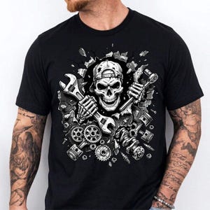 May include: Black t-shirt featuring a detailed graphic of a skull wearing a backwards baseball cap, holding wrenches and surrounded by engine parts. The design has a mechanic theme, with gears, pistons, and other tools.