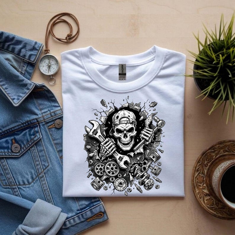 May include: White t-shirt featuring a black and white graphic of a skull wearing a cap and holding wrenches. The design includes gears, pistons, and a cracked wall effect, suggesting a mechanic theme.