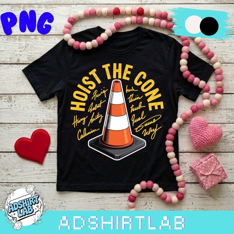 May include: Black t-shirt with the text "HOIST THE CONE" in yellow, featuring an orange and white traffic cone graphic. Additional text includes names in a handwritten style. The shirt is displayed with decorative items.