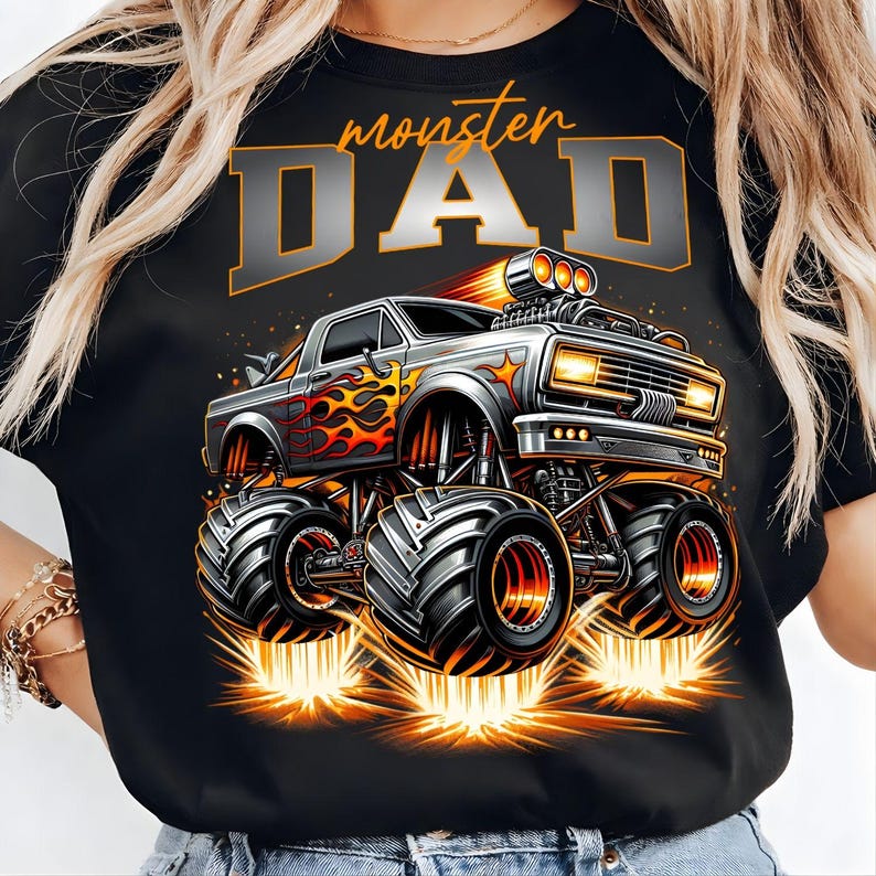 Pode incluir: T-shirt preto com um design de monster truck, chamas e o texto "monster DAD" em laranja e prata. O caminh&atilde;o tem pneus grandes e emite fa&iacute;scas. Um design divertido para um pai.