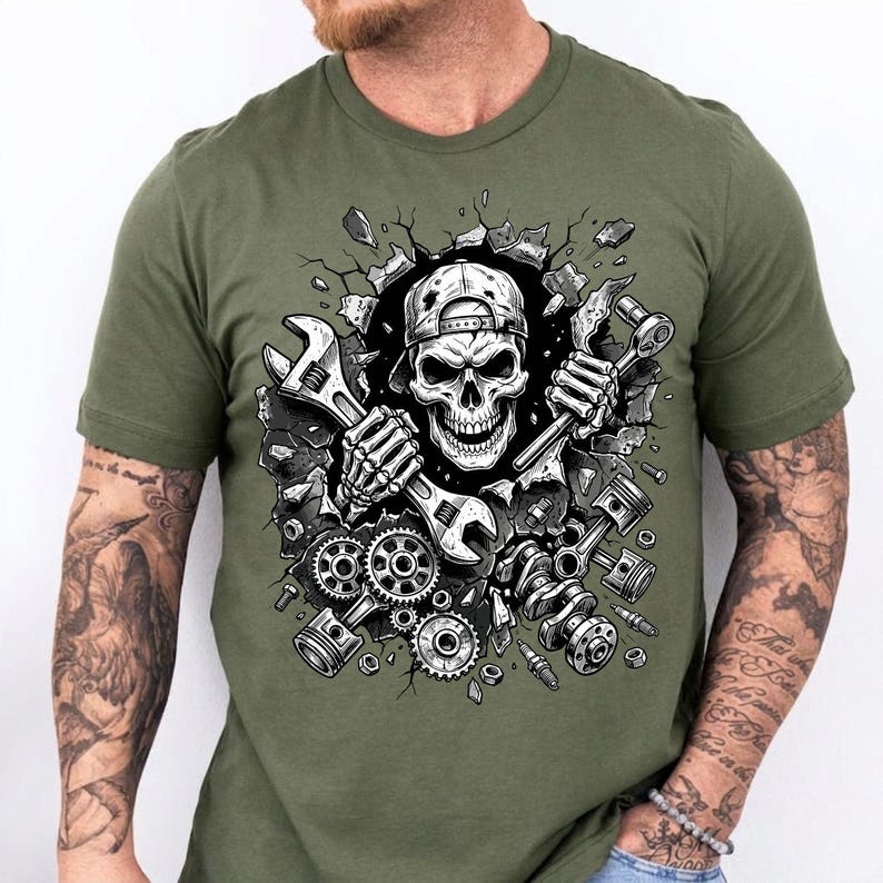May include: Olive green t-shirt featuring a detailed graphic of a skull wearing a backwards baseball cap, holding wrenches. The skull is breaking through a wall, surrounded by engine parts. A unique design for mechanics and automotive enthusiasts.