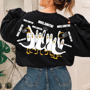 May include: Black sweatshirt featuring a graphic of cartoon seagulls with the text "MRS. SMITH!". The seagulls are white with black wings and yellow feet. The text is in white.
