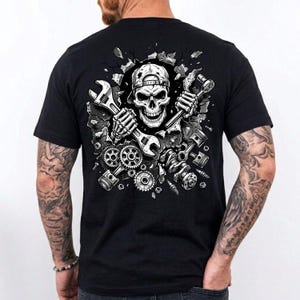 May include: Black t-shirt featuring a detailed graphic of a skull wearing a cap, holding wrenches, and surrounded by engine parts. The design is in shades of gray and white, with a cracked wall effect. A unique design for mechanics and car enthusiasts.