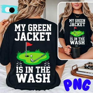 May include: Black t-shirt with the text "MY GREEN JACKET IS IN THE WASH" in white. The shirt features a golf-themed graphic with a green putting green, a golf ball, a golf club, and a red flag.
