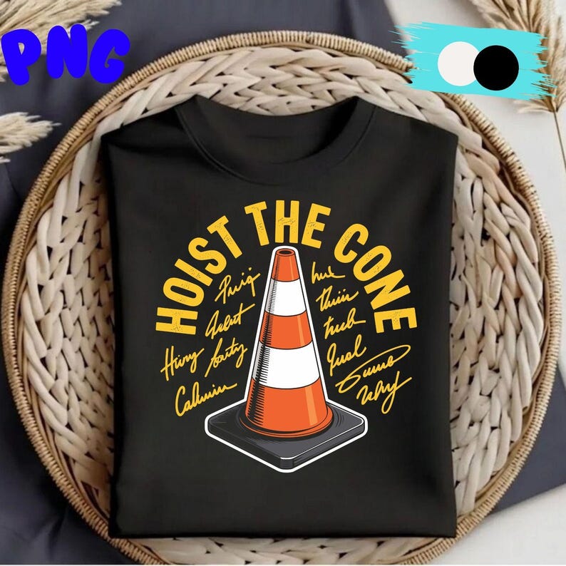 May include: Black t-shirt with the text "HOIST THE CONE" in yellow, surrounding a graphic of an orange and white traffic cone. The shirt is displayed in a woven basket.