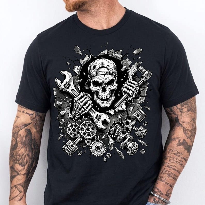 May include: Black t-shirt featuring a detailed graphic of a skull wearing a cap and holding wrenches. The skull is breaking through a wall, surrounded by engine parts like gears, pistons, and a crankshaft. The design is in shades of gray and white.