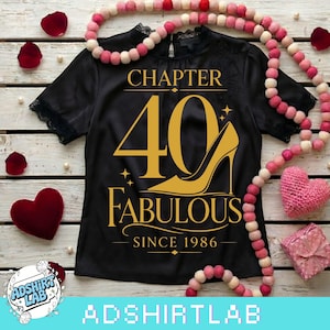 Può includere: T-shirt nero con testo dorato "CAPITOLO 40 FAVOLOSO DAL 1986" e grafica di un tacco alto. La maglietta è decorata con bordi in pizzo e circondata da elementi decorativi, tra cui un cuore rosa e petali di rosa.