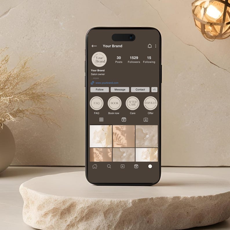 May include: A smartphone displaying a social media profile for "Your Brand," a salon. The profile shows a logo, follower count, and various service options. The phone is dark brown and rests on a light-colored, textured stone pedestal.