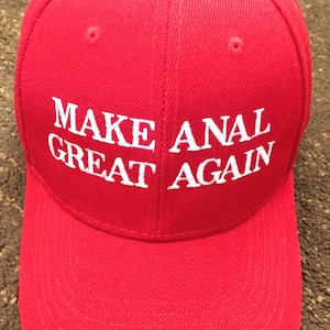 May include: A red baseball cap with the phrase "MAKE ANAL GREAT AGAIN" in white capital letters. The cap has a curved brim and a structured crown with ventilation eyelets.