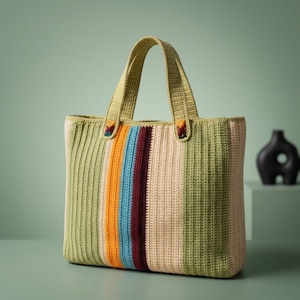 Può includere: Una borsa tote rettangolare all'uncinetto con strisce verticali nei toni del verde salvia, arancione brillante, azzurro, bordeaux intenso e crema. La borsa ha due manici all'uncinetto in verde salvia abbinati con piccoli accenti colorati.