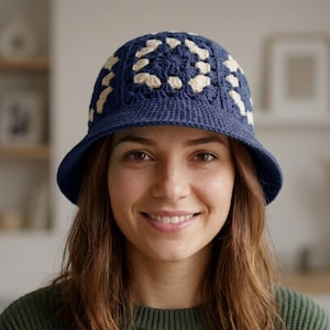 May include: A crochet bucket hat featuring a dark blue base with a cream-colored granny square pattern around the crown. The hat has a solid dark blue brim and a textured, hand-stitched appearance, crafted from yarn with a visible woven structure.