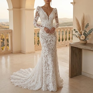 May include: A white lace wedding dress with long sleeves and a V-neck. The dress has a mermaid cut and a long train. The intricate floral lace pattern is visible. The background shows a balcony with a scenic view.