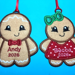 May include: Two felt gingerbread person ornaments with red ribbon loops. The left figure wears a red bow tie with the name Andy and the year 2026 embroidered. The right figure wears a green glitter bow and a red polka dot dress with Becca and 2026.