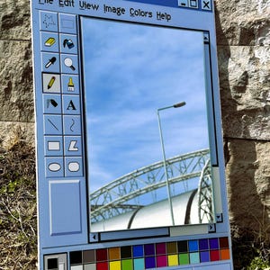 Può includere: Specchio azzurro progettato per assomigliare all'interfaccia dell'applicazione Paint di Windows. Lo specchio riflette un cielo blu, un lampione e una struttura metallica. Il testo "untitled - Paint" è in alto, con altre opzioni di menu e icone.