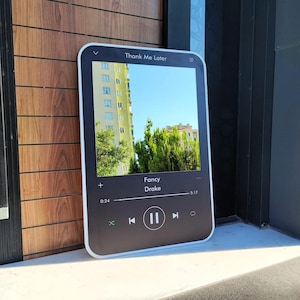 May include: A rectangular black plaque featuring a white border and a digital music player interface. The screen displays the text Thank Me Later, Fancy, and Drake, with a progress bar showing 0:24 of 5:17, playback controls, and a photo of a building.
