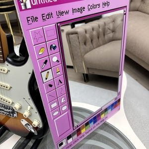 May include: A pink framed mirror designed to resemble the classic "Untitled - Paint" application window. The mirror features a color palette and menu options like "File Edit View Image Colors Help". A guitar is visible in the background.