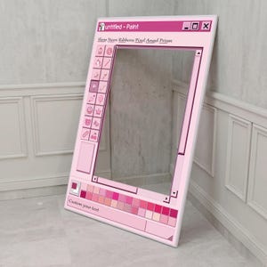 Può includere: Un supporto rosa per cabina fotografica a forma di finestra di computer, con la scritta "untitled - Paint" in alto. L'accessorio presenta una tavolozza di colori, icone e la scritta "Custom your text" in basso. Il telaio è appoggiato a un muro.