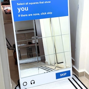 May include: A rectangular floor mirror featuring a white frame with a blue header displaying the text "Select all squares that show you" and "If there are none, click skip". The mirror surface is divided into a three-by-three grid, with a blue "SKIP" button.