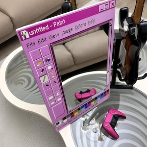 May include: A pink mirror in the shape of a computer window, with the text "Untitled - Paint" at the top. The mirror reflects a pink game controller. The window design includes a toolbar with icons and the text "File Edit View Image Colors Help".