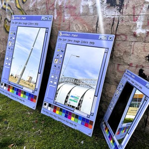 Puede incluir: Tres espejos grandes con marco azul claro apoyados contra una pared de ladrillos cubierta de graffiti. Los espejos est&aacute;n dise&ntilde;ados para parecerse a la interfaz cl&aacute;sica del programa Paint de Windows, con una paleta de colores y una barra de men&uacute;. Los reflejos muestran escenas al aire libre.