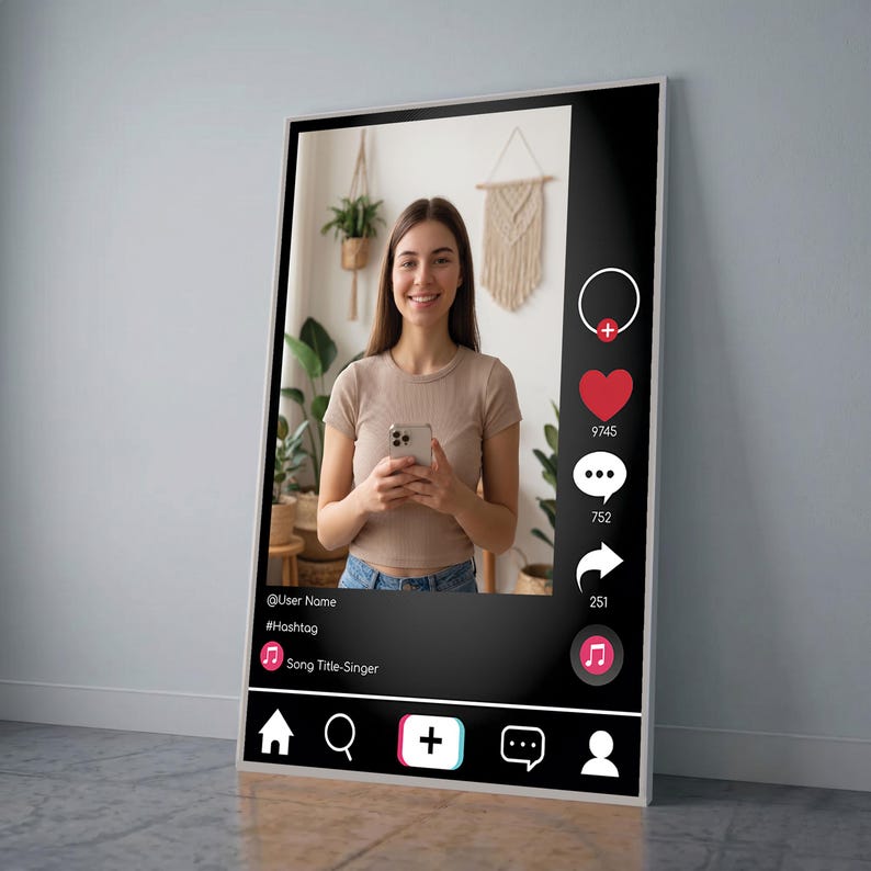 Op de afbeelding: Een ingelijste poster met een social media-interface met een vrouw die een smartphone vasthoudt. De zwarte interface bevat een profielpictogram, een hart, een commentaarbubbel en een deelpictogram. De poster heeft een witte rand en leunt tegen een grijze muur.